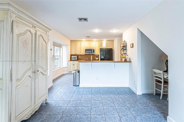 kitchen with backsplash, kitchen peninsula, a breakfast bar area, black fridge with ice dispenser, and light tile patterned floors