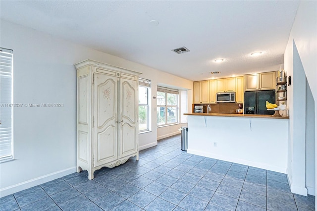 kitchen with backsplash, dark tile patterned flooring, a textured ceiling, black fridge with ice dispenser, and a breakfast bar area