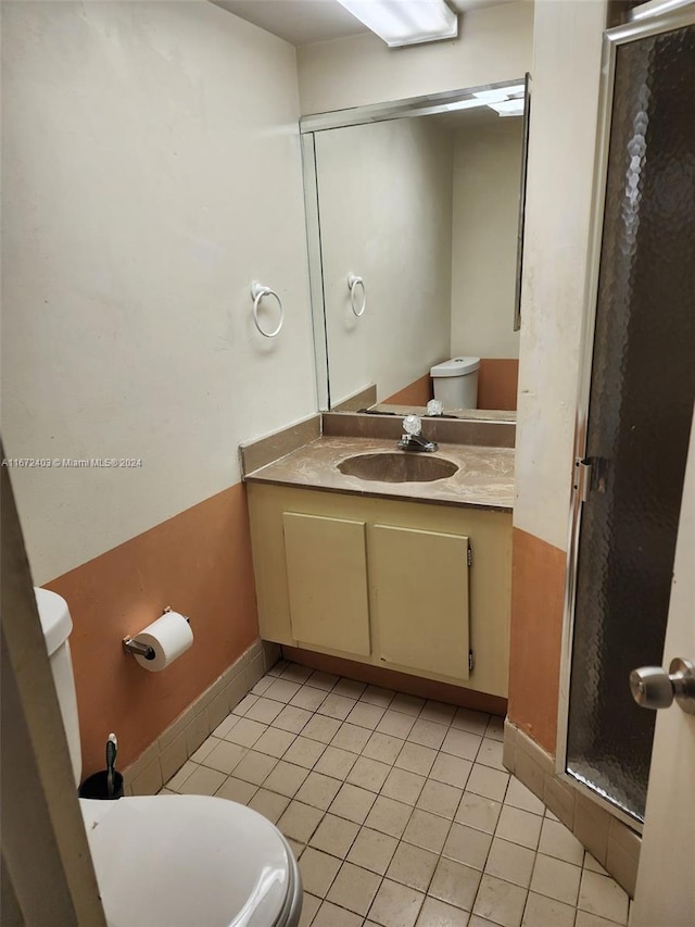 bathroom with a shower with door, vanity, toilet, and tile patterned floors