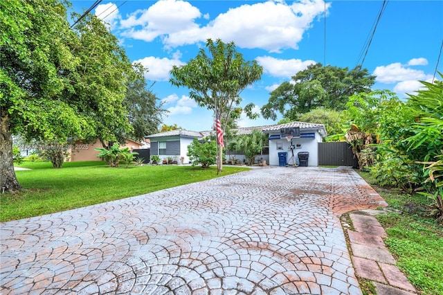 view of front of home with a tile roof, fence, decorative driveway, a front lawn, and stucco siding