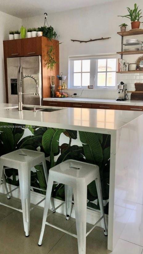 kitchen featuring stainless steel fridge, a breakfast bar, backsplash, and tile patterned floors