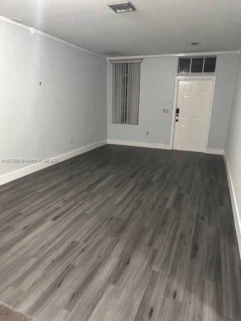 empty room with dark hardwood / wood-style floors and crown molding