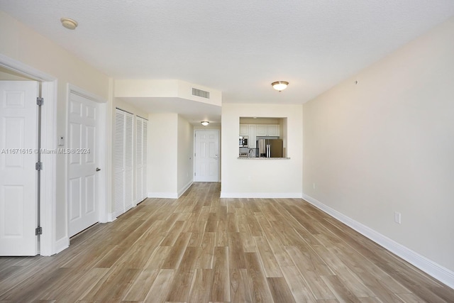 unfurnished living room with light wood-type flooring and a textured ceiling