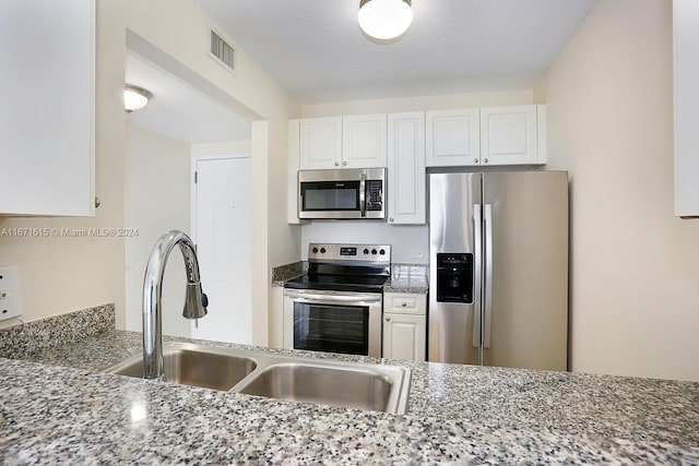 kitchen featuring a textured ceiling, white cabinetry, stainless steel appliances, and light stone counters