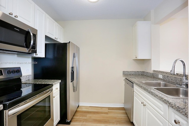 kitchen with light stone counters, light hardwood / wood-style floors, sink, white cabinets, and appliances with stainless steel finishes