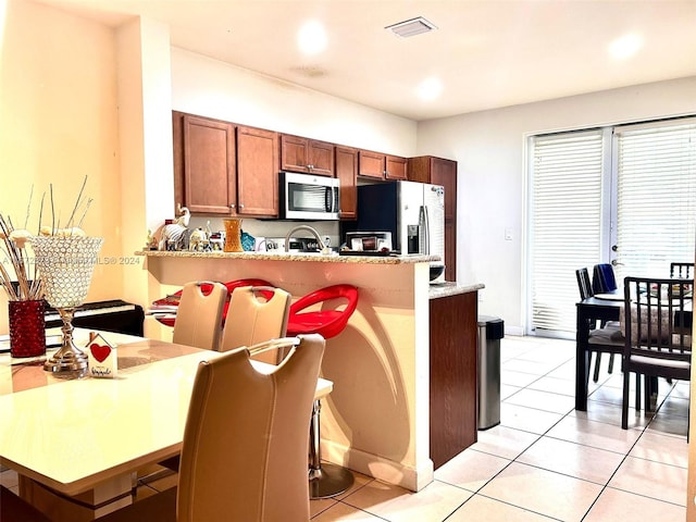 kitchen with kitchen peninsula, light tile patterned floors, a breakfast bar, and appliances with stainless steel finishes