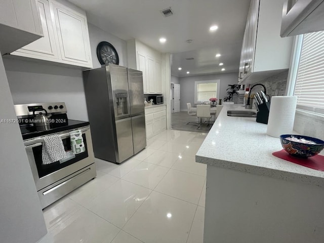 kitchen with light tile patterned flooring, sink, white cabinetry, appliances with stainless steel finishes, and light stone countertops