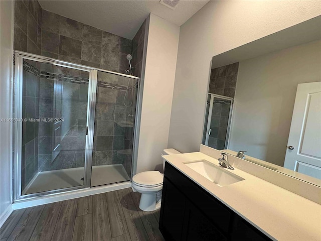 bathroom with a textured ceiling, hardwood / wood-style flooring, walk in shower, vanity, and toilet