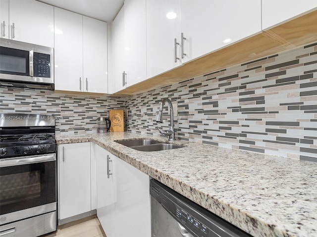 kitchen with white cabinetry, sink, stainless steel appliances, tasteful backsplash, and light stone counters