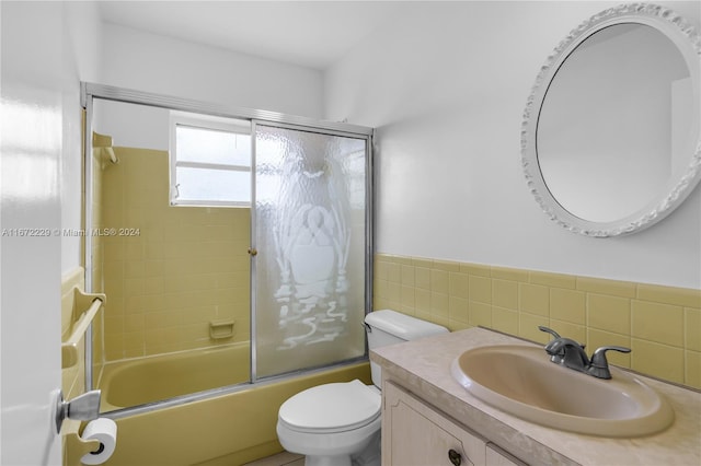 full bathroom featuring vanity, toilet, shower / bath combination with glass door, and tile walls