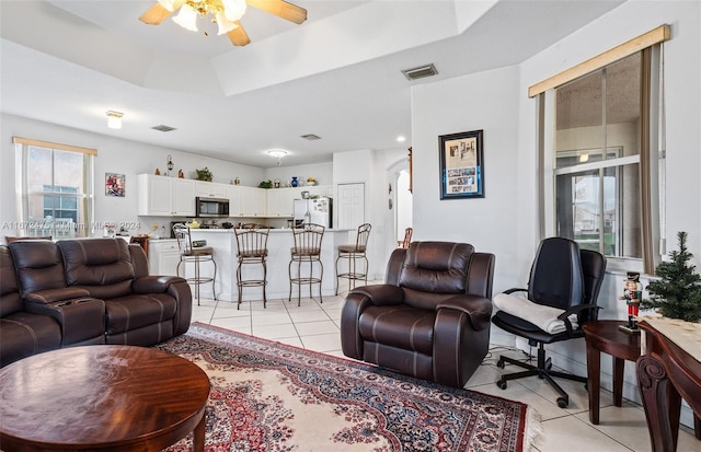 tiled living room with a tray ceiling and ceiling fan