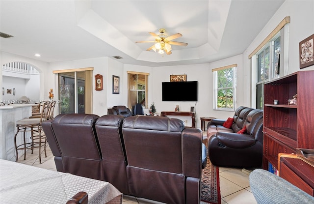 living room featuring light tile patterned floors, ceiling fan, and a raised ceiling