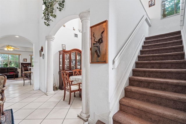 stairs with a towering ceiling, tile patterned flooring, decorative columns, and ceiling fan