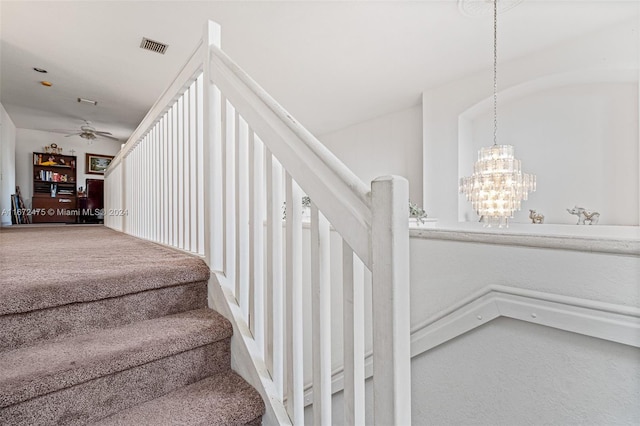 stairway with carpet and ceiling fan with notable chandelier