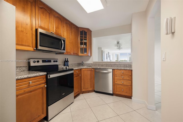 kitchen with light tile patterned flooring, sink, stainless steel appliances, and light stone counters