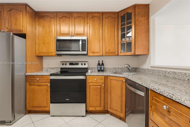 kitchen with light stone countertops, stainless steel appliances, light tile patterned floors, and sink