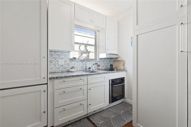 kitchen with light stone countertops, white cabinetry, stainless steel oven, and tasteful backsplash