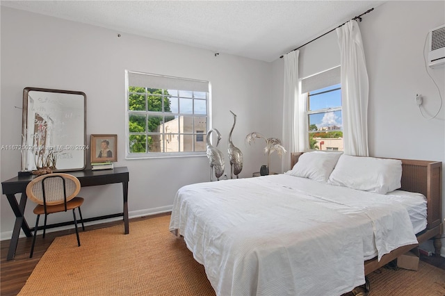 bedroom featuring wood-type flooring, a textured ceiling, multiple windows, and an AC wall unit