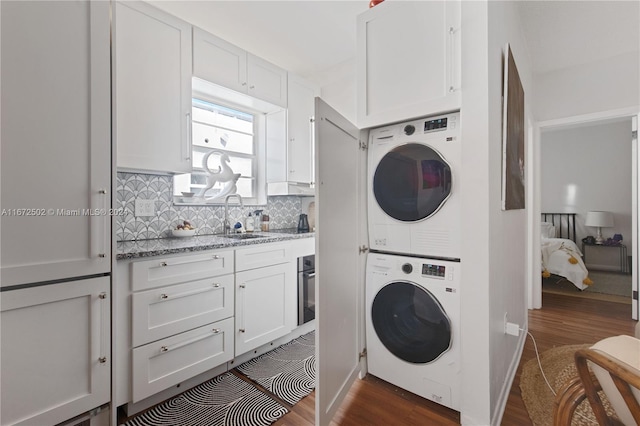 washroom featuring dark wood-type flooring, sink, and stacked washing maching and dryer