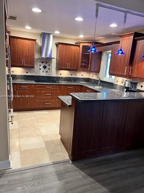 kitchen with light wood-type flooring, sink, kitchen peninsula, wall chimney range hood, and decorative light fixtures