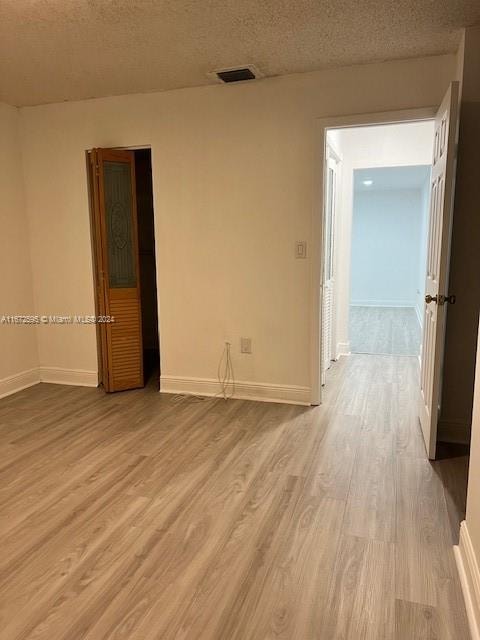 spare room featuring light wood-type flooring and a textured ceiling