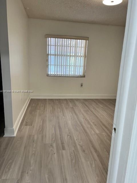 empty room with a textured ceiling and light hardwood / wood-style flooring