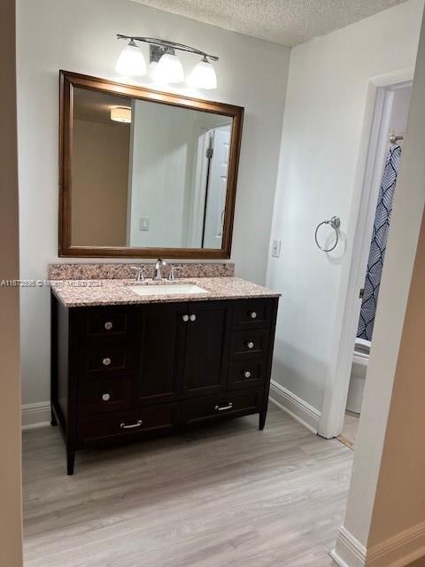 bathroom with a textured ceiling, hardwood / wood-style flooring, vanity, and toilet