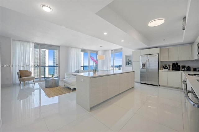 kitchen with a center island, tasteful backsplash, stainless steel refrigerator with ice dispenser, a raised ceiling, and light tile patterned floors