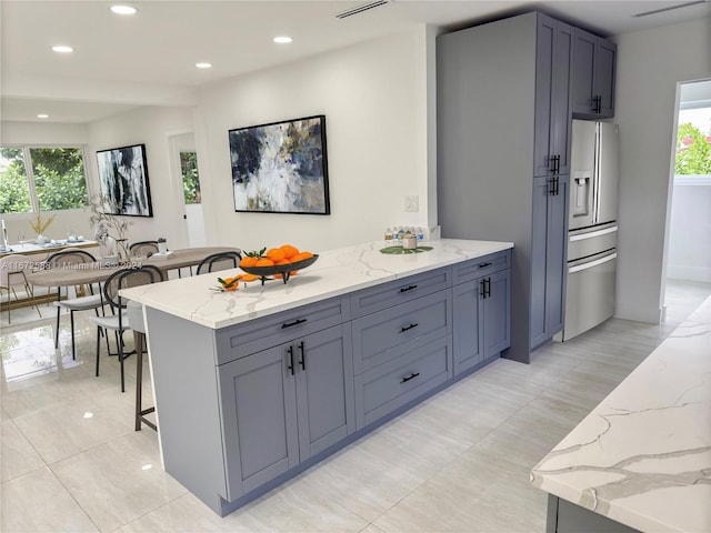 kitchen with gray cabinetry, a breakfast bar, light stone countertops, and stainless steel fridge with ice dispenser