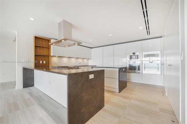 kitchen with island range hood, appliances with stainless steel finishes, kitchen peninsula, and white cabinetry