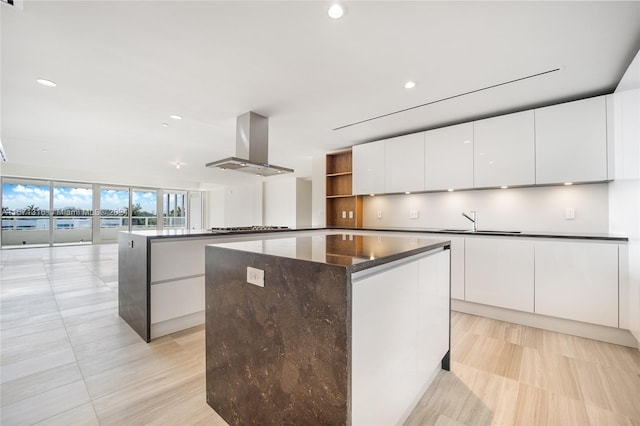 kitchen with white cabinets, wall chimney exhaust hood, sink, and a kitchen island