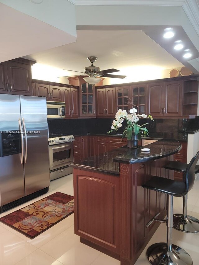 kitchen with dark brown cabinetry, stainless steel appliances, a kitchen breakfast bar, and ceiling fan