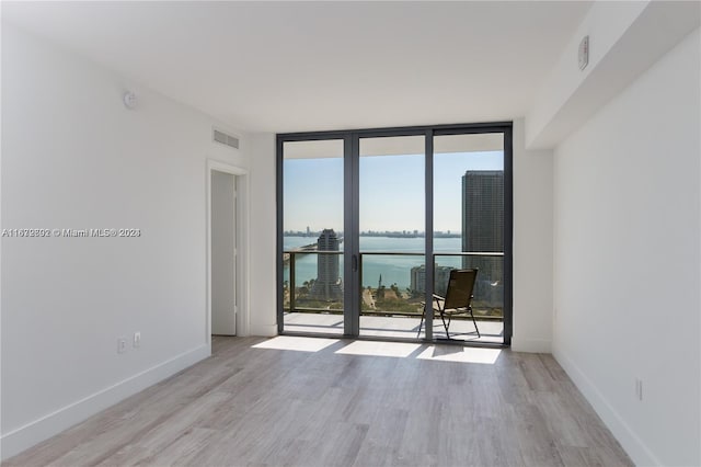 unfurnished room featuring expansive windows, light hardwood / wood-style floors, and a water view