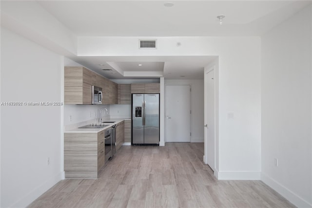 kitchen featuring appliances with stainless steel finishes, a raised ceiling, and light wood-type flooring