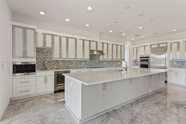 kitchen featuring wine cooler, built in appliances, sink, and an island with sink