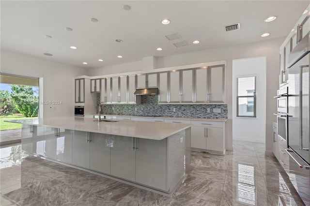 kitchen featuring sink, gray cabinets, a breakfast bar, a spacious island, and decorative backsplash