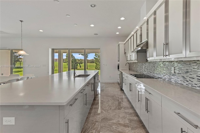 kitchen with pendant lighting, sink, tasteful backsplash, a large island with sink, and black electric stovetop