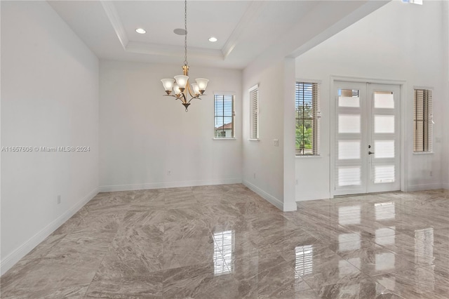 spare room with ornamental molding, a tray ceiling, an inviting chandelier, and french doors