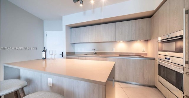 kitchen with sink, light tile patterned floors, a kitchen breakfast bar, light brown cabinetry, and cooktop