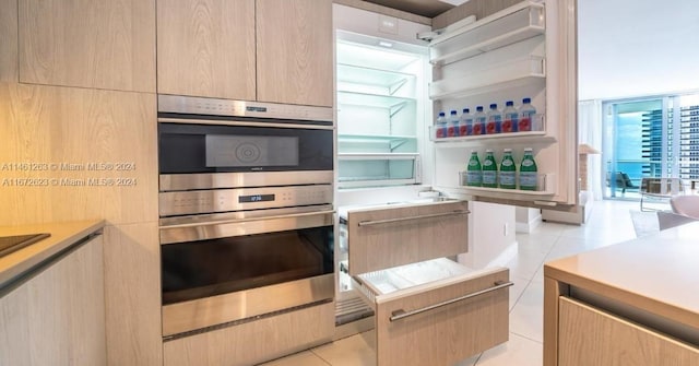 kitchen with stainless steel double oven, light brown cabinetry, and light tile patterned floors