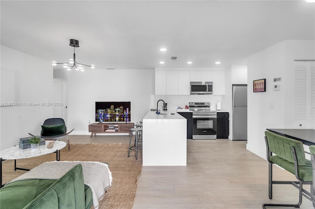 kitchen featuring white cabinets, hanging light fixtures, sink, light hardwood / wood-style flooring, and stainless steel appliances