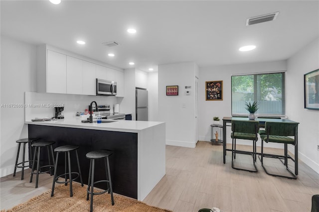 kitchen with a kitchen bar, white cabinets, appliances with stainless steel finishes, and kitchen peninsula