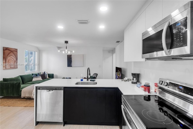 kitchen featuring pendant lighting, sink, white cabinetry, stainless steel appliances, and light hardwood / wood-style floors