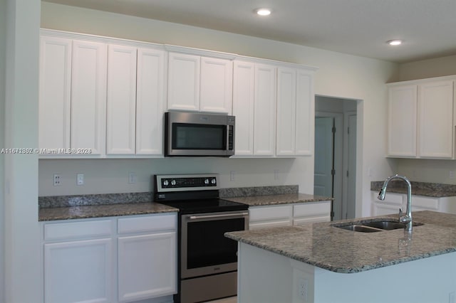 kitchen with a kitchen island with sink, stainless steel appliances, sink, and white cabinetry