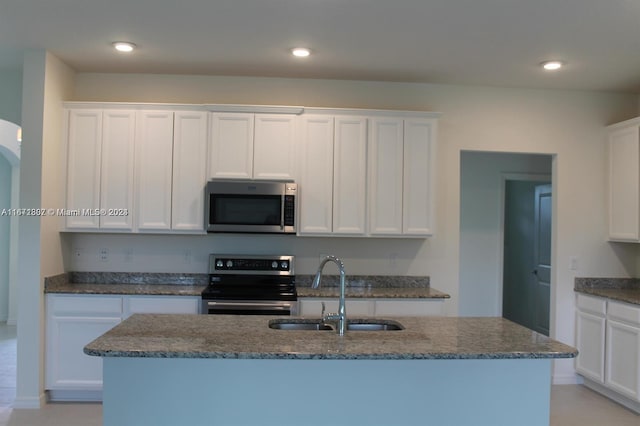 kitchen featuring a kitchen island with sink, sink, white cabinets, stainless steel appliances, and dark stone countertops