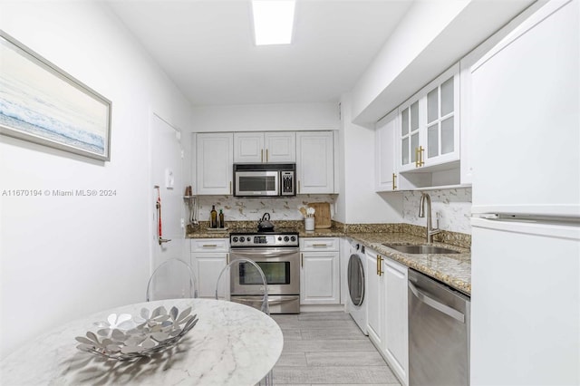 kitchen featuring washer / dryer, sink, white cabinetry, appliances with stainless steel finishes, and light stone countertops