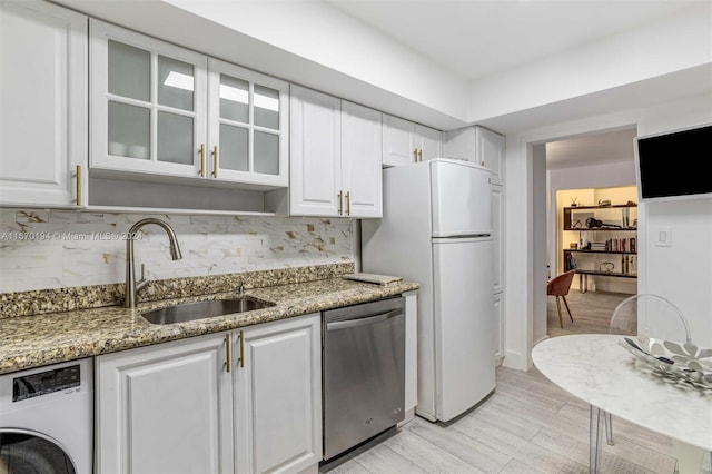 kitchen featuring appliances with stainless steel finishes, white cabinetry, light stone counters, washer / dryer, and sink