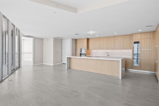 kitchen with sink, stainless steel double oven, a kitchen island, decorative backsplash, and light brown cabinetry