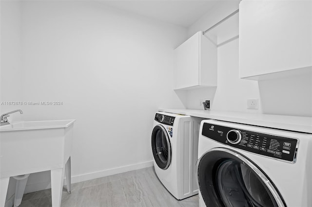 clothes washing area featuring cabinets, light wood-type flooring, and washer and clothes dryer