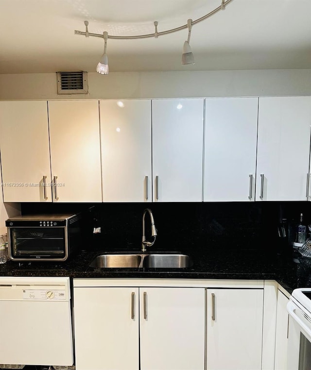 kitchen with dark stone counters, white cabinetry, white appliances, and sink